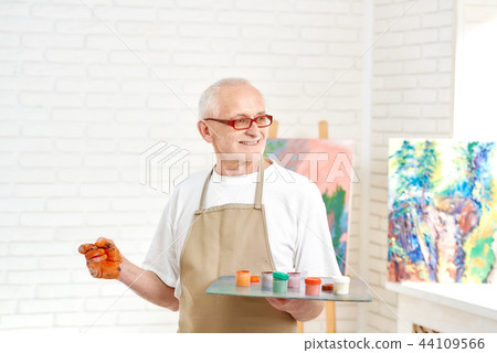 Senior male painter, standing with palette of colors in hand at studio. Senior male painter, standing with palette of colors in hand at studio. 44109566