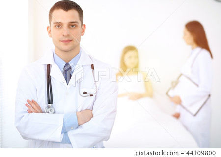 Medicine doctor standing and smiling on the background with patient in the bed Medicine doctor standing and smiling on the background with patient in the bed 44109800
