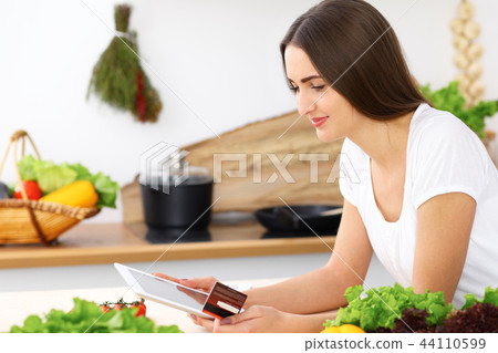 Beautiful Hispanic  woman cooking while using tablet computer in kitchen or  making online shopping 44110599