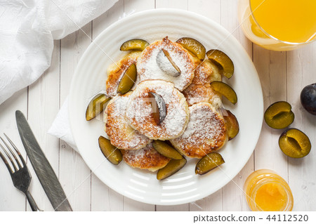 Cheese pancakes in powdered sugar with fresh plums Cheese pancakes in powdered sugar with fresh plums 44112520