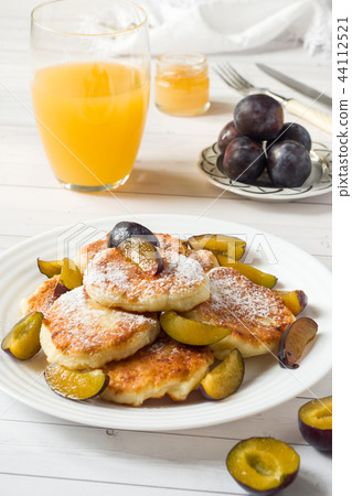 Cheese pancakes in powdered sugar with fresh plums Cheese pancakes in powdered sugar with fresh plums 44112521