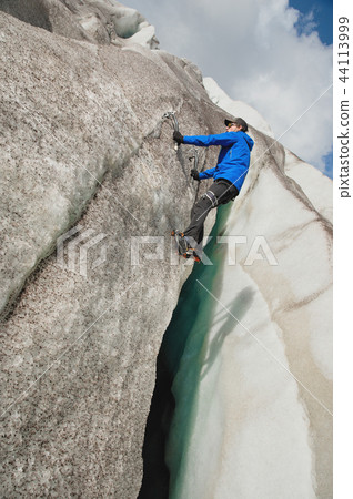 A free climber without insurance with two ice axes rises from a crack in the glacier. Free climbing A free climber without insurance with two ice axes rises from a crack in the glacier. Free climbing 44113999