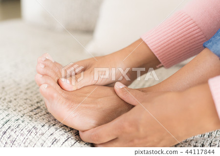 Woman sitting on sofa holds her foot injury Woman sitting on sofa holds her foot injury 44117844