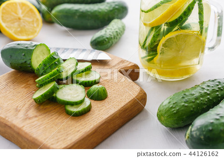 Cutting board with sliced cucumbers for detox water. Process of preparing energy cocktail Cutting board with sliced cucumbers for detox water. Process of preparing energy cocktail 44126162