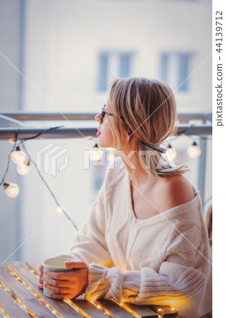 Young woman with cup of coffee near fairy lights  44139712