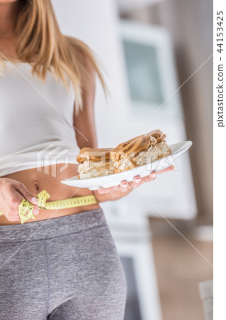 Woman holding plate with cakes and measure tape. 44153425