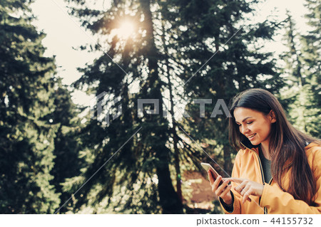 Charming girl using smartphone in sunny coniferous wood Charming girl using smartphone in sunny coniferous wood 44155732