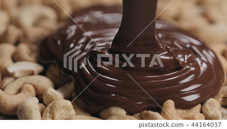 closeup covering roasted cashew with melted dark chocolate closeup covering roasted cashew with melted dark chocolate 44164037
