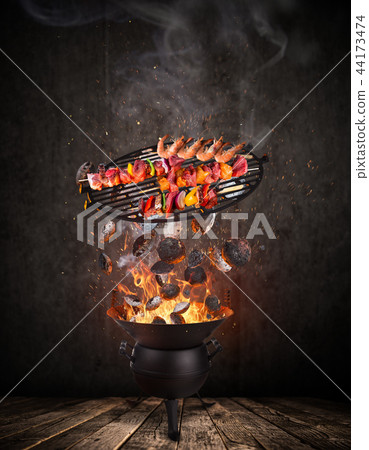 Kettle grill with hot briquettes, cast iron grate and tasty skewers flying in the air. Kettle grill with hot briquettes, cast iron grate and tasty skewers flying in the air. 44173474