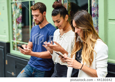 Group of three people looking down at smart phone smiling Group of three people looking down at smart phone smiling 44180842