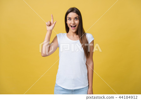 Amaze young woman pointing to one side with her finger while opening her mouth against a yellow Amaze young woman pointing to one side with her finger while opening her mouth against a yellow 44184912