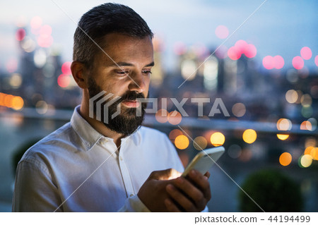 A businessman with smartphone at sunset, text messaging. 44194499