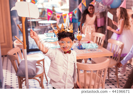 Little boy wearing paper crown and putting hand up at the party Little boy wearing paper crown and putting hand up at the party 44196671