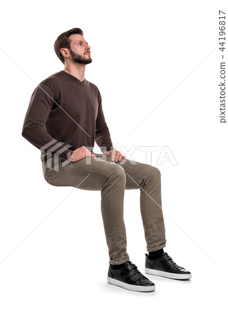 An isolated bearded man in casual wear sits on a white background with hands on his thighs and looks 44196817