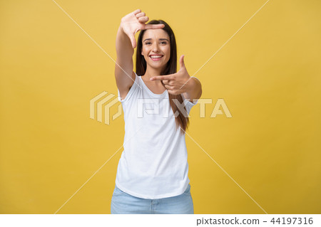 Young beautiful woman over isolated yellow background smiling making frame with hands and fingers Young beautiful woman over isolated yellow background smiling making frame with hands and fingers 44197316