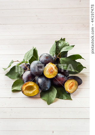 Fresh plum fruit with leaves on a light table. 44197478