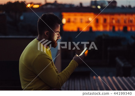 Young man is standing on the roof of the house and reading message. 44199340