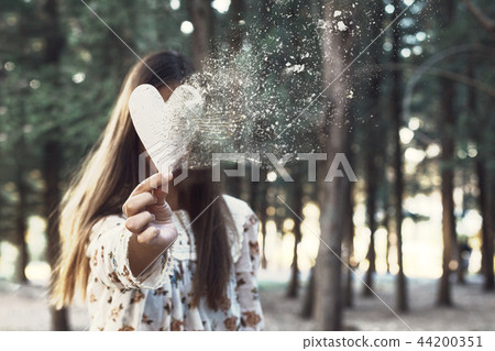Conceptual woman portrait with dispersion effect of a heart in her hand 44200351