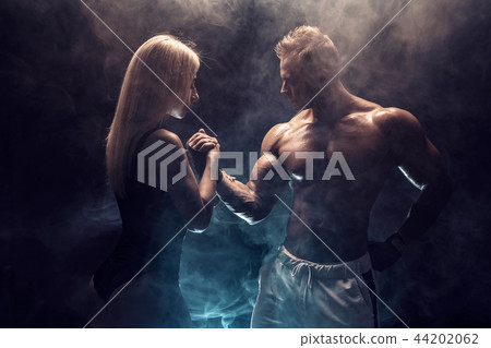 Attractive couple, a slim blonde female and handsome shirtless guy posing at studio on a dark 44202062