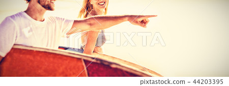 Happy man with woman gesturing while carrying sunrfboard at beach 44203395