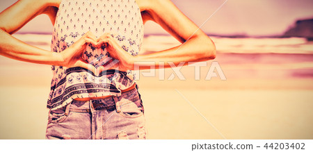 Mid section of woman making heart shape with hands at beach 44203402