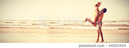 Side view of man lifting woman at beach 44203434