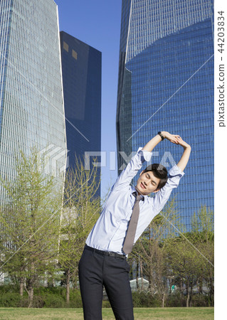 Cheerful young businessman walking in park near office building in the background. Spend time in park with collegue near office. 286 Cheerful young businessman walking in park near office building in the background. Spend time in park with collegue near office. 286 44203834
