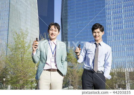 Cheerful young businessman walking in park near office building in the background. Spend time in park with collegue near office. 306 Cheerful young businessman walking in park near office building in the background. Spend time in park with collegue near office. 306 44203835