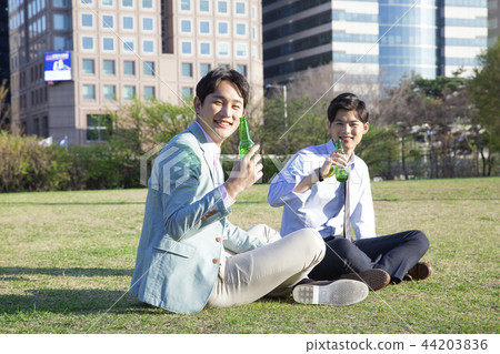 Cheerful young businessman walking in park near office building in the background. Spend time in park with collegue near office. 310 44203836