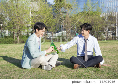 Cheerful young businessman walking in park near office building in the background. Spend time in park with collegue near office. 307 44203946