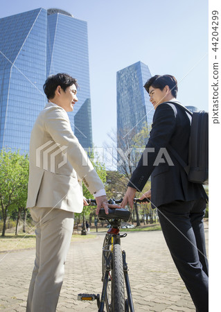 Cheerful young businessman walking in park near office building in the background. Spend time in park with collegue near office. 193 44204299
