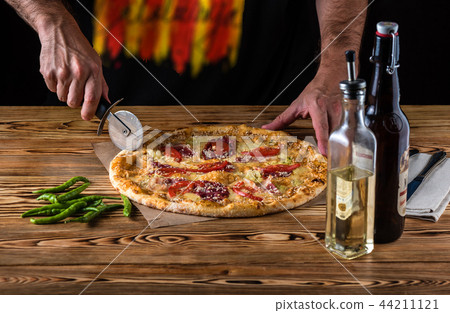 The guy cuts pizza on a wooden table 44211121