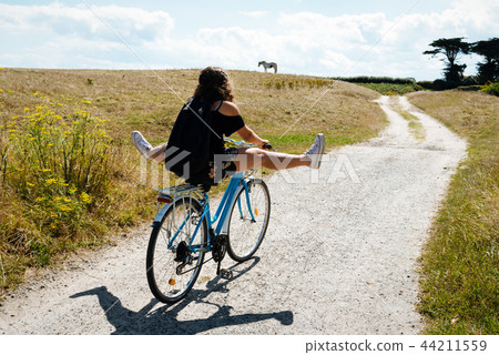 Pretty young woman riding bicycle in a country road  44211559