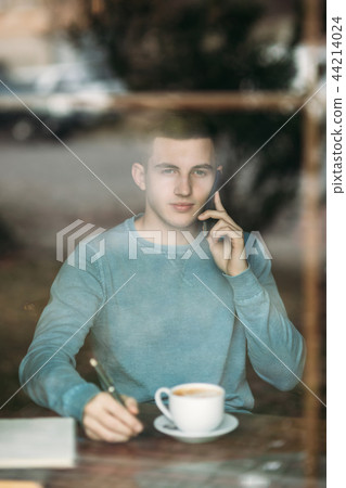 Man with phone in a cafe sits opposite the window. Talking on the phone. View from the window 44214024