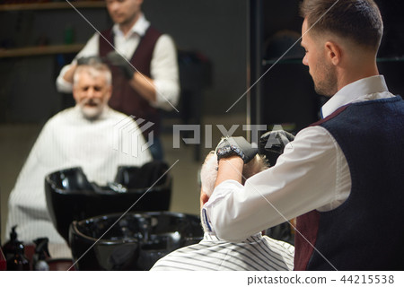 Barber in black gloves grooming and styling haircut of client. 44215538