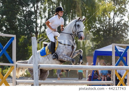 Equestrian sport. Young girl jumping over obstacle 44217743