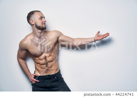 Smiling muscular shirtless man directing an arm at blank copy space 44224741