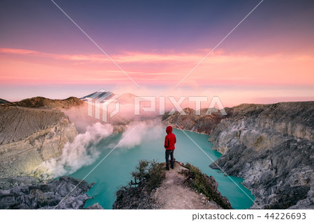 Man standing on edge of crater with colorful sky 44226693