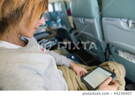 Woman reading ebook sitting inside airplane Woman reading ebook sitting inside airplane 44230407
