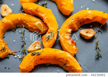 Cooked pumpkin pieces with garlic and rosemary on a black plate. Copy spase. 44238981