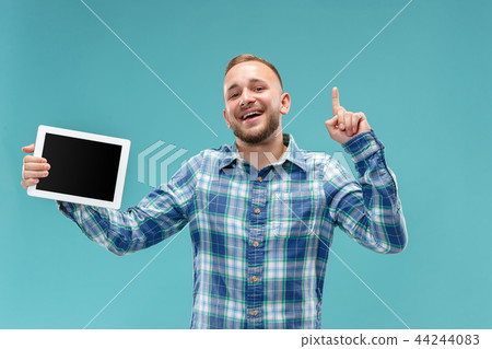 Studio picture of positive man isolated on blue background standing in casual clothes holding tablet Studio picture of positive man isolated on blue background standing in casual clothes holding tablet 44244083