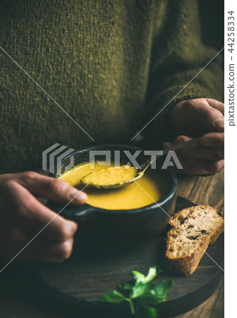 Man in winter sweater eating sweet corn soup from bowl 44258334