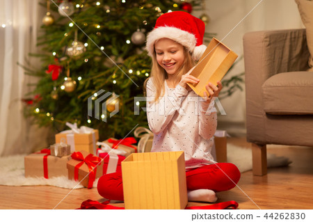 smiling girl in santa hat opening christmas gift 44262830