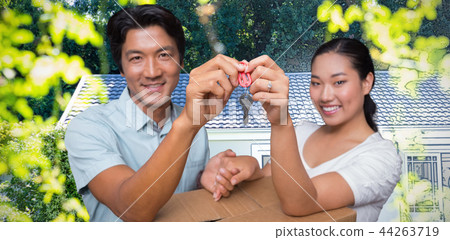 Composite image of happy couple holding house key and leaning on moving box Composite image of happy couple holding house key and leaning on moving box 44263719