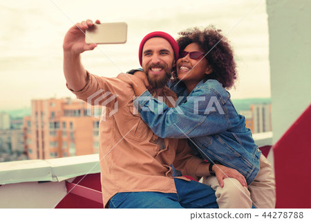 Emotional curly girl hugging her boyfriend while taking selfies with him 44278788