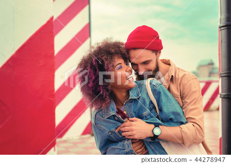 Bearded young man standing behind his beautiful girlfriend and hugging her Bearded young man standing behind his beautiful girlfriend and hugging her 44278947