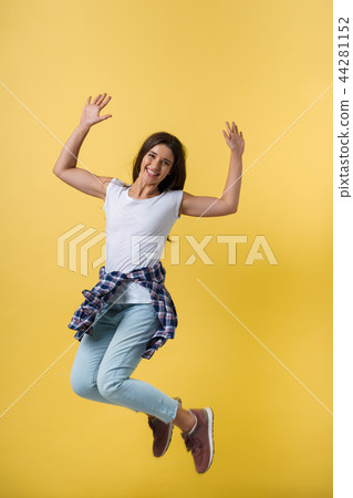 Full-length portrait of carefree girl in white shirt and jean jumping on yellow background. 44281152
