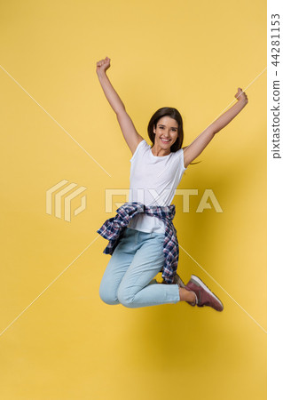 Full-length portrait of carefree girl in white shirt and jean jumping on yellow background. 44281153