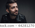 Attractive young man with a modern trendy hairstyle posing against a dark grey background with 44281270