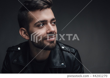 Attractive young man with a modern trendy hairstyle posing against a dark grey background with 44281270